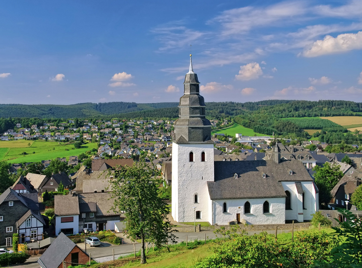 Prosoz Herten-Bild Startseite Eversberg ProBAUG- ländliche Landschaft mit Häusern und einer weißen Kirche mit Turm